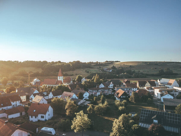 This stock photo shows a small town surrounded by fields and hills. The houses are mostly white with red roofs. The photo has a clear and sunny sky. german village photo drone shoot.