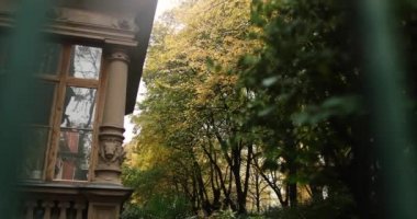 Old stone building guarded by green iron fence with autumn trees. High quality 4k footage