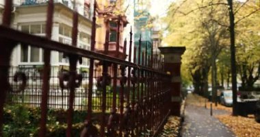 Following red fence leading to old city buildings with golden autumn trees. High quality 4k footage