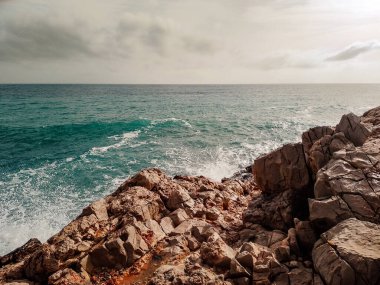 Fırtınalı mavi denizin manzarası kayalık sahilden bulutlu gökyüzünün altında