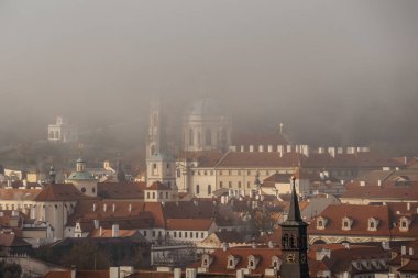 Çek Cumhuriyeti 'nin sisli sonbahar sabahında Prag panoraması. Aziz Niklas Kilisesi, tarihi binaları ve kırmızı çatıları olan küçük bir kasaba. Avrupa şehir manzarası. Seyahat mimarisi kavramı.