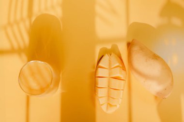 Üst ve düz yaz meyveleri tropikal yaprak gölgesi ve sarı arka planda mango dilimi ve meyve suyu ile uzanır.