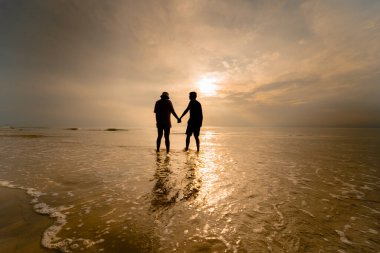 Siluet Asyalı çift yaz aylarındaki balayı aktivitesinden mutluluk ve neşe içinde el ele tutuşuyorlar.