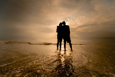 Siluet Asyalı çift yaz aylarındaki balayı aktivitesinden mutluluk ve neşe içinde el ele tutuşuyorlar.