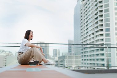 Tek başına yaşayan Asyalı kadın açık havada nefes al ve şehrin arka planında çatıda rahatla.