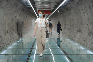 İşe giderken ya da seyahat ederken koruyucu maske takan tek başına bir Asyalı kadın.