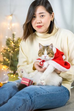 Asyalı kadın gülüyor ve oyun sırasında mutlu ve kedisine kırmızı Noel Baba battaniyesi giyiyor.