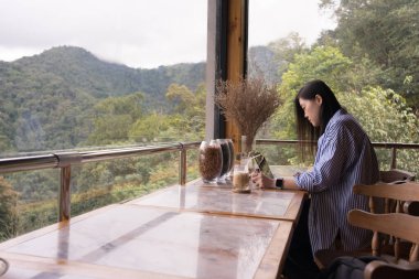 Dijital göçebe konsepti Asyalı serbest çalışan kadın dağ manzaralı kahve dükkanında çalışmak için dizüstü bilgisayar kullanıyor.