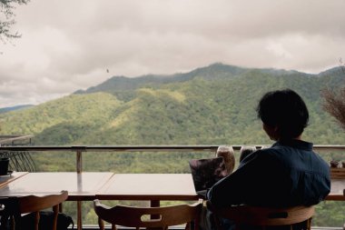 Dijital göçebe konsepti Asyalı serbest çalışan adam dağ manzaralı kahve dükkanında çalışmak için dizüstü bilgisayar kullanıyor.