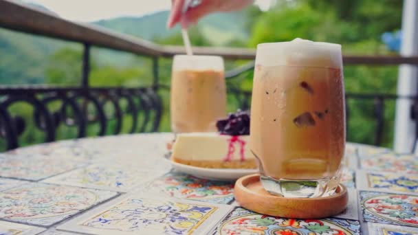 山の景色を背景にコーヒーショップの屋外でアイスコーヒーを混ぜながらスローモーションウーマンハンドで人々の活動コンセプト — ストック動画