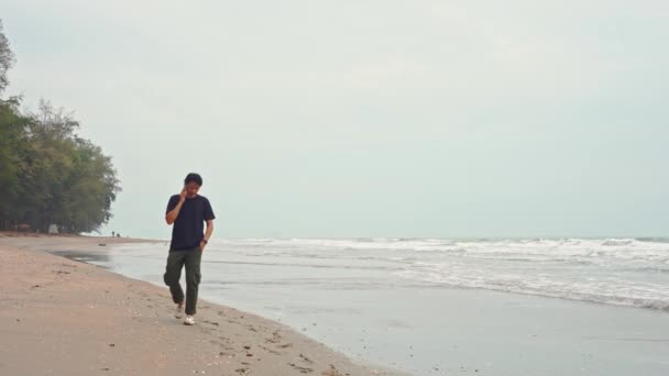 人々の活動コンセプト アジア人男性と波のゆっくり動く移動と海の背景を持つ砂浜で携帯電話を使用して — ストック動画