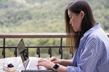 Dijital göçebe konsepti Asyalı serbest çalışan kadın akıllı telefon kullanır. Kahve dükkanında dağdan dağa fotoğraf çeker.