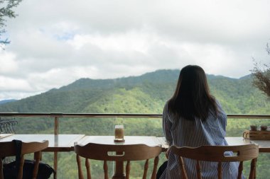 Dijital göçebe konsepti Asyalı serbest çalışan kadın rahatlayıp dağ manzaralı kahve dükkanında çalışıyor.