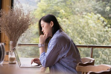 Dijital göçebe konsepti Asyalı serbest çalışan kadın dağ manzaralı kahve dükkanında çalışmak için dizüstü bilgisayar kullanıyor.