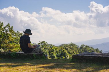 landscape and travel concept with solo freelancer man sit on wooden and use tablet work from outdoor with layer of mountain background