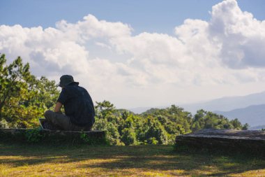 landscape and travel concept with solo freelancer man sit on wooden and use tablet work from outdoor with layer of mountain background