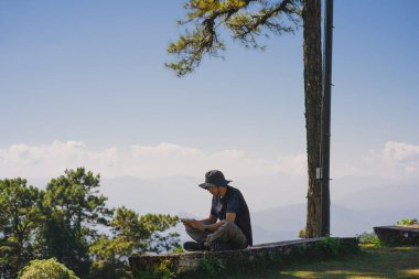 landscape and travel concept with solo freelancer man sit on wooden and use tablet work from outdoor with layer of mountain background