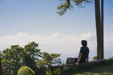 landscape and travel concept with solo freelancer man sit on wooden and use tablet work from outdoor with layer of mountain background