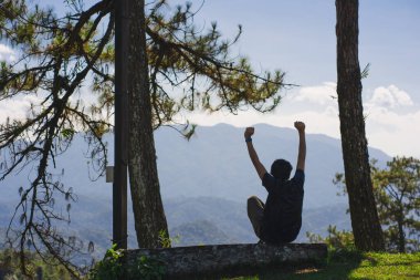 landscape and travel concept with solo freelancer man sit on wooden and use tablet work from outdoor with layer of mountain background