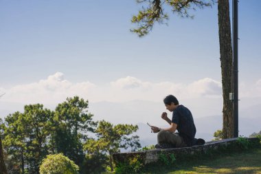 landscape and travel concept with solo freelancer man sit on wooden and use tablet work from outdoor with layer of mountain background