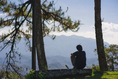 landscape and travel concept with solo freelancer man sit on wooden and use tablet work from outdoor with layer of mountain background