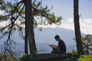 landscape and travel concept with solo freelancer man sit on wooden and use tablet work from outdoor with layer of mountain background