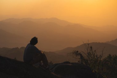 Tek başına serbest çalışan bir adamla manzara ve seyahat kavramı dağın tepesinde ve dağ katmanıyla gün batımında rahatlar.
