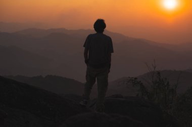 Tek başına serbest çalışan bir adamla manzara ve seyahat kavramı dağın tepesinde ve dağ katmanıyla gün batımında rahatlar.