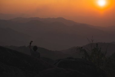 Tek başına serbest çalışan bir adamla manzara ve seyahat kavramı dağın tepesinde ve dağ katmanıyla gün batımında rahatlar.