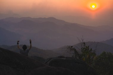 Tek başına serbest çalışan bir adamla manzara ve seyahat kavramı dağın tepesinde ve dağ katmanıyla gün batımında rahatlar.