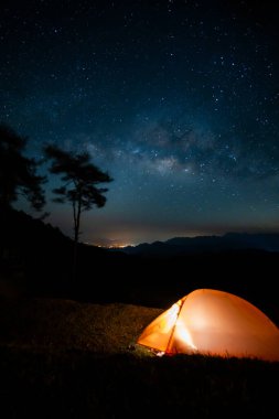 Doğa, samanyolu arka planına sahip dağda turuncu kamp çadırıyla seyahat ediyor.