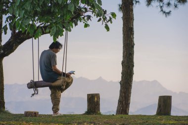 peyzaj ve seyahat konsepti tek başına çalışan bir adam büyük bir ağaç ve dağ katmanı altında salıncak ahşap tablet iş kullanın