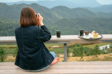 solo asian woman hipster traveler taking photo to mountain at outdoor bar of coffeeshop clipart