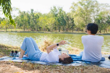 Asyalı çift piknik yapıyor ve rahatlıyor. Parkta, gölde, ilkbaharda mutlulukla.