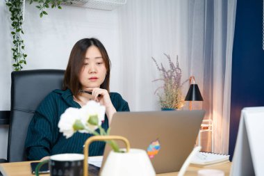 Asyalı kadın işini evden yürütmek için dizüstü bilgisayar kullanıyor.