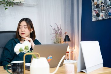 Asyalı kadın işini evden yürütmek için dizüstü bilgisayar kullanıyor.