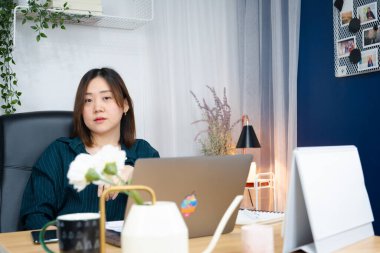 Asyalı kadın işini evden yürütmek için dizüstü bilgisayar kullanıyor.