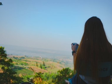 Tek başına seyahat eden bir kadın oturur ve dağ manzaralı bir kahve içer.