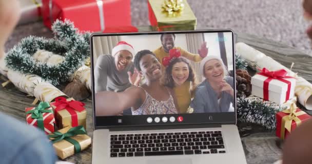幸せな多様な友人とラップトップビデオ通話を持つサンタの帽子を持つ多様な友人 クリスマス お祭り 通信技術 — ストック動画