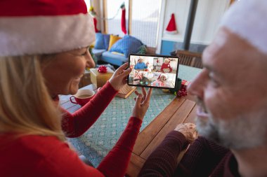 Üst düzey Kafkasyalı çift çeşitli insanlarla yılbaşı videosu çekiyor. İletişim teknolojisi ve noel, dijital kompozit görüntü.