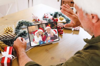 Kafkasyalı kıdemli bir adam Kafkasyalı bir aileyle Noel 'de görüntülü görüşme yapıyor. İletişim teknolojisi ve noel, dijital kompozit görüntü.