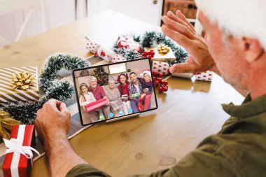 Kafkasyalı kıdemli bir adam Kafkasyalı bir aileyle Noel 'de görüntülü görüşme yapıyor. İletişim teknolojisi ve noel, dijital kompozit görüntü.