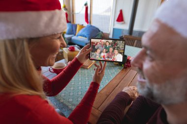 Kafkasyalı üst düzey bir çift Kafkasyalı bir aileyle Noel 'de görüntülü görüşme yapıyor. İletişim teknolojisi ve noel, dijital kompozit görüntü.