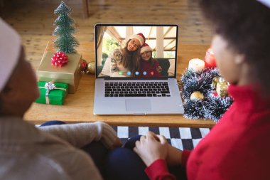 Afrikalı Amerikalı çift, Kafkasyalı kadın ve kızıyla Noel 'de görüntülü görüşme yapıyor. İletişim teknolojisi ve noel, dijital kompozit görüntü.