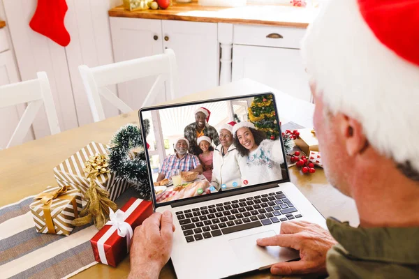 アフリカ系アメリカ人の家族とクリスマスのビデオ通話を持っているシニア白人男性 通信技術とクリスマス デジタル複合画像 — ストック写真