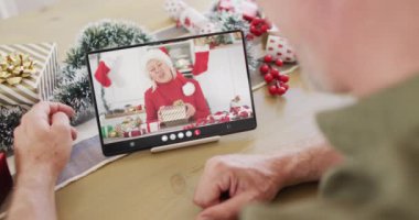 Kafkasyalı bir adam Noel süslemeleri ile mutlu beyaz bir kadınla tablet video görüşmesi yapıyor. Noel, şenlik ve iletişim teknolojisi.