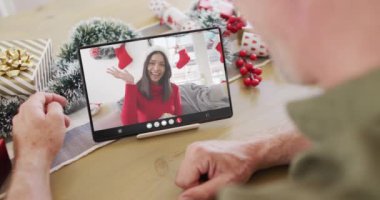 Kafkasyalı bir adam, Noel süslemeleri ile melez bir kadınla tablet video görüşmesi yapıyor. Noel, kutlama, dijital kompozit video.