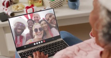 Noel Baba şapkalı Afrikalı Amerikalı bir kadın mutlu arkadaşlarıyla dizüstü bilgisayar görüşmesi yapıyor. Noel, gelenek ve kutlama konsepti, dijital kompozit video.