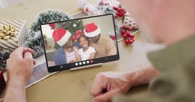Kafkasyalı bir adam Noel süslemeleri ile mutlu Afro-Amerikan ailesiyle tablet video görüşmesi yapıyor. Noel, şenlik ve iletişim teknolojisi.