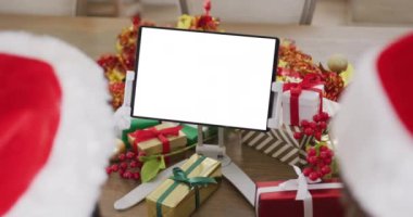Noel Baba şapkalı beyaz çift fotokopi odasıyla tablet görüntülü görüşme yapıyorlar. Noel, şenlik ve iletişim teknolojisi.